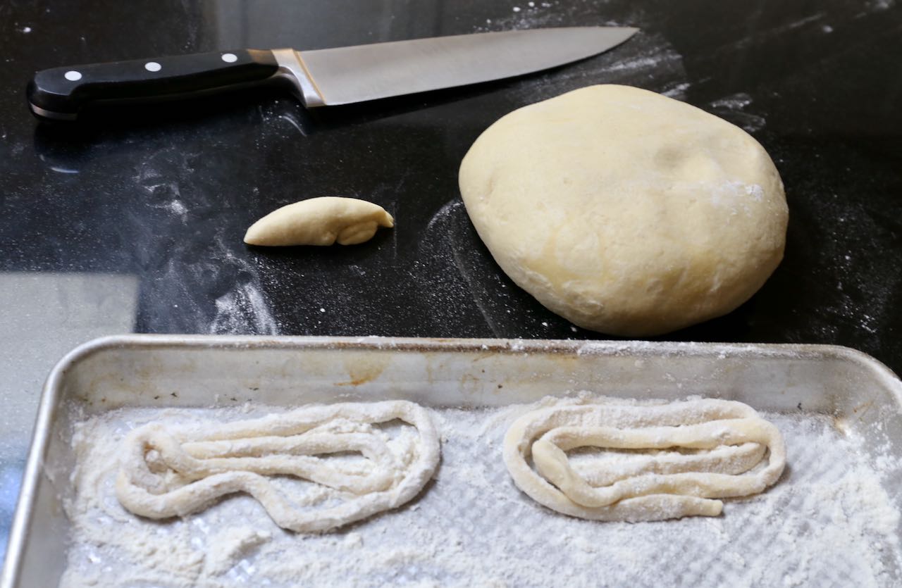 Slice pieces of pici pasta dough and prepare a flour dusted baking sheet.