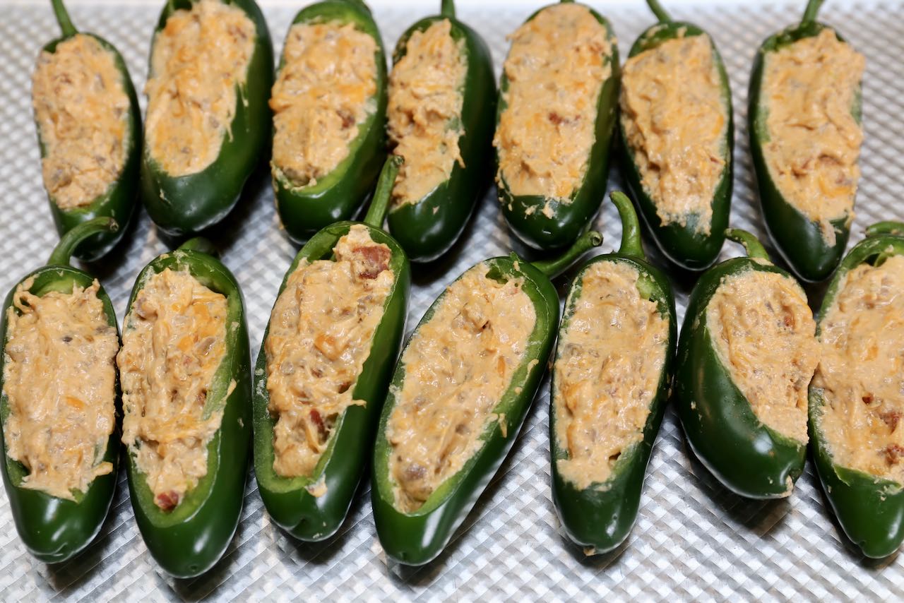 Use a small spoon to scoop cheese filling into jalapeno peppers on a baking sheet. 
