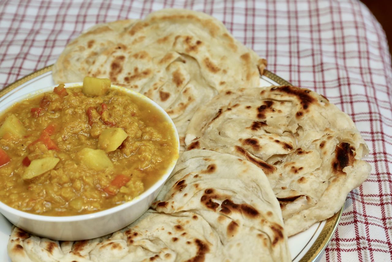 Tear flaky flatbread and use it to scoop roti canai curry sauce.