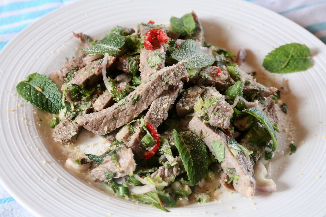 Nam Tok Beef Salad is garnished with spicy Thai red chili. 