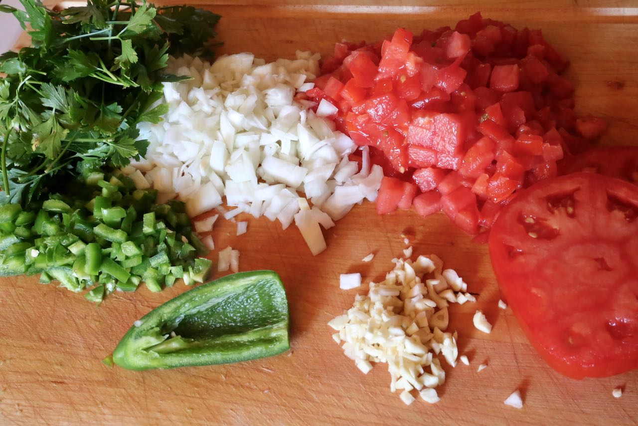 Being preparing Ezme Salata by chopping garlic, tomato, onion, peppers and parsley.