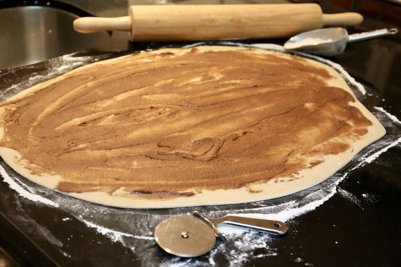 Roll Kardemummabullar dough onto a floured surface and spread with cardamom and cinnamon filling.