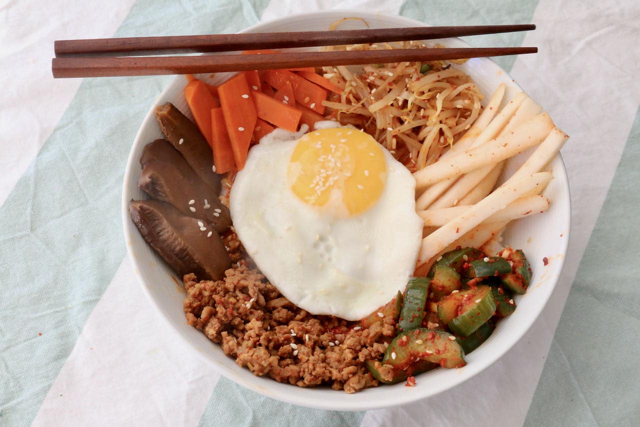 Serve Pork Bibimbap garnished with sesame seeds and use chopsticks to mix all the ingredients together. 