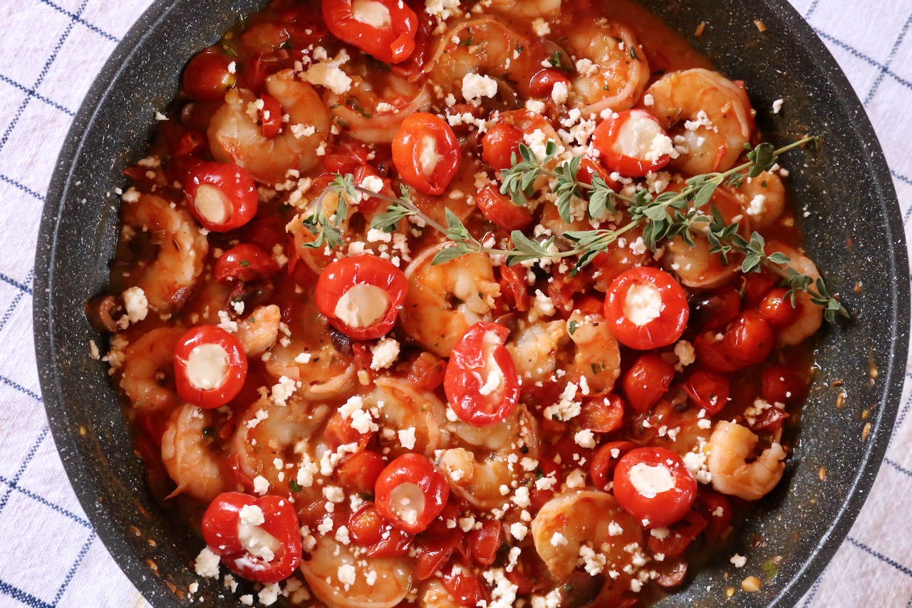 Serve Shrimp Saganaki garnished with cheese stuffed peppers and oregano sprigs.