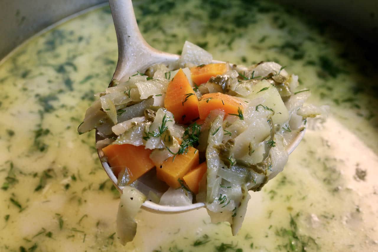 Use a ladle to transfer Ogorkowa Zupa into soup bowls.