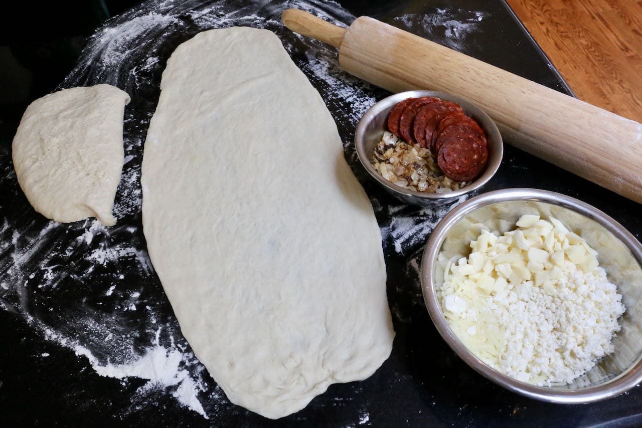 Use a rolling pin to roll out Peynirli Pide dough into an oval shape.