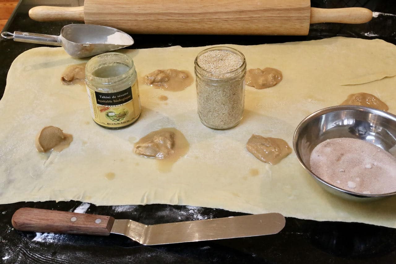 Using a rolling pin to stretch out the dough then slather with tahini sesame paste.