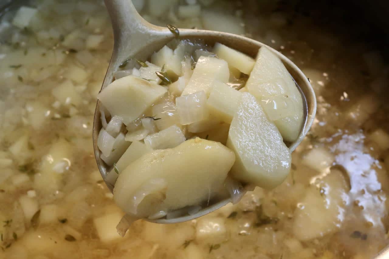 Use a ladle to transfer cooked Parsnip and Pear Soup into a blender.