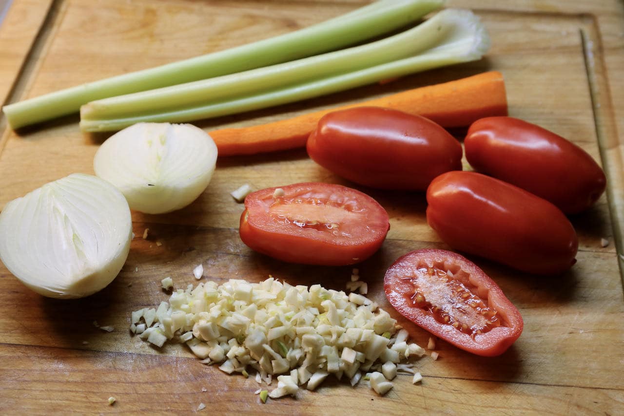 Being preparing homemade Mexican Bean Soup by chopping garlic, onions, celery, carrots and tomatoes.