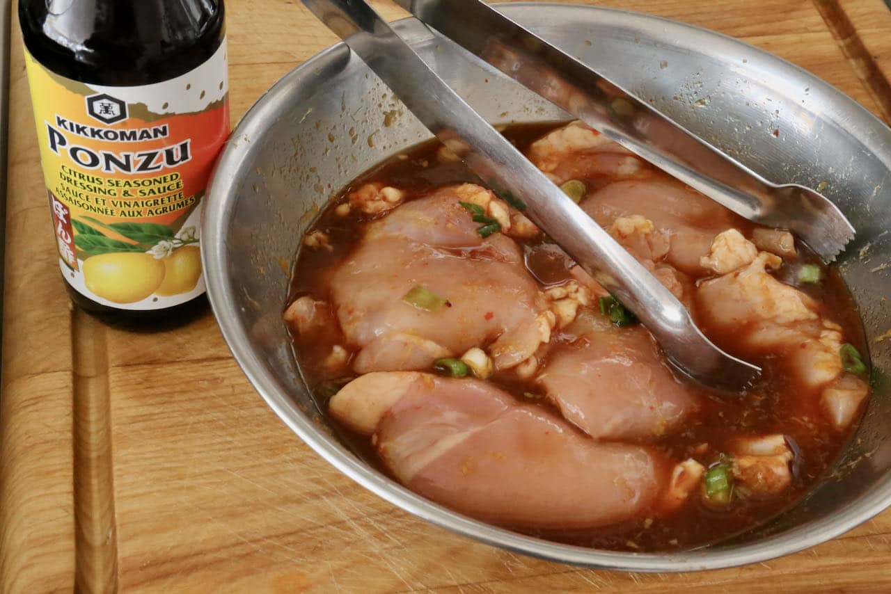 Use tongs to transfer marinated Ponzu chicken thighs to a wok or skillet.