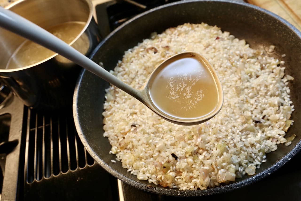 Slowly add warm vegetable stock to arborio rice while stirring to make a creamy risotto.