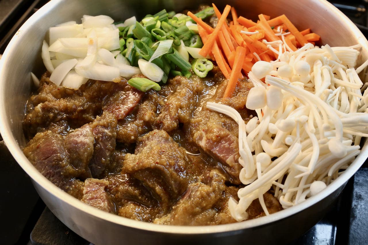 Cook the marinated Beef Bulgogi in a pot with onions, scallions, carrots, and enoki mushrooms.
