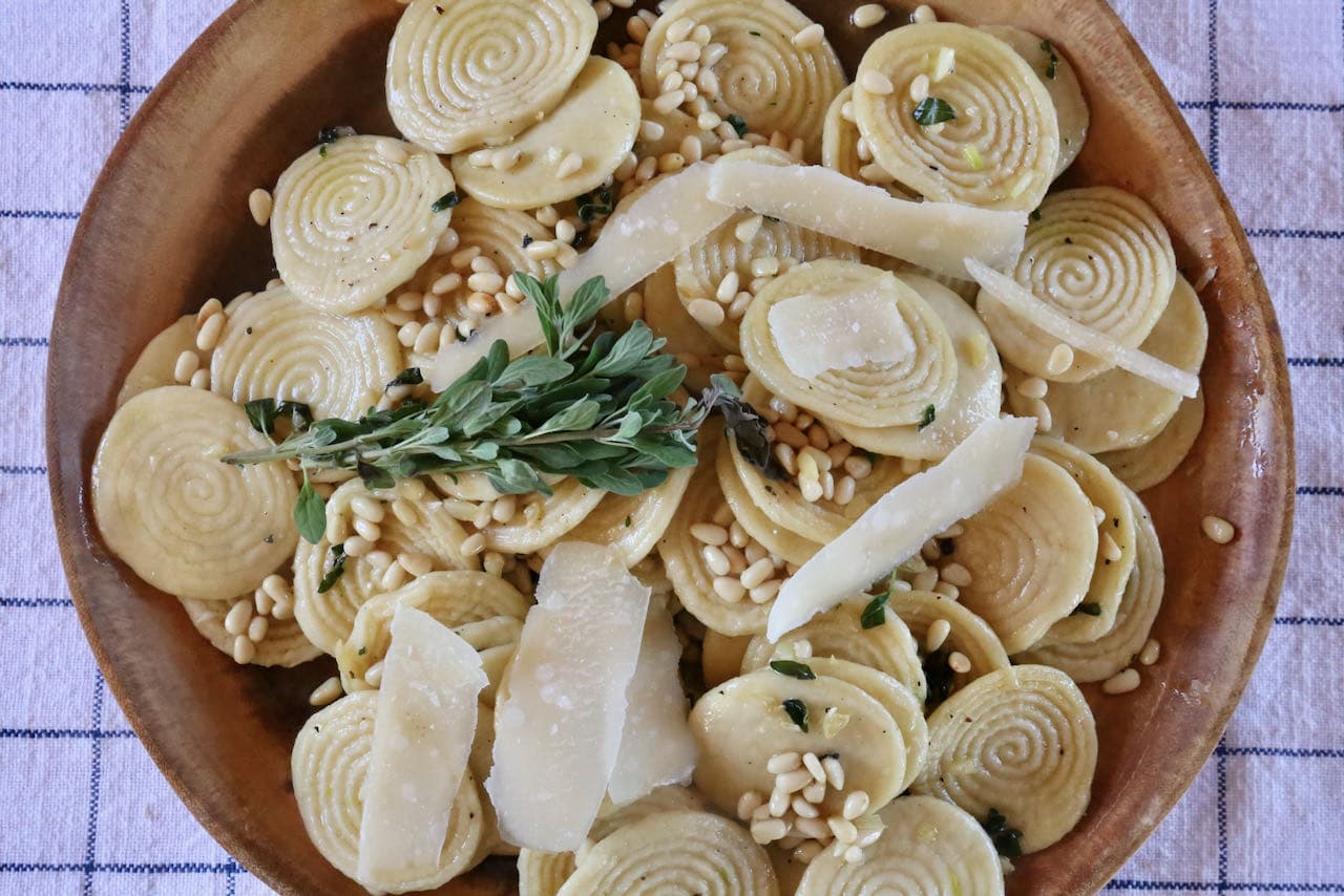 Top Corzetti with marjoram sprigs, toasted pine nuts and shaved parmesan cheese.