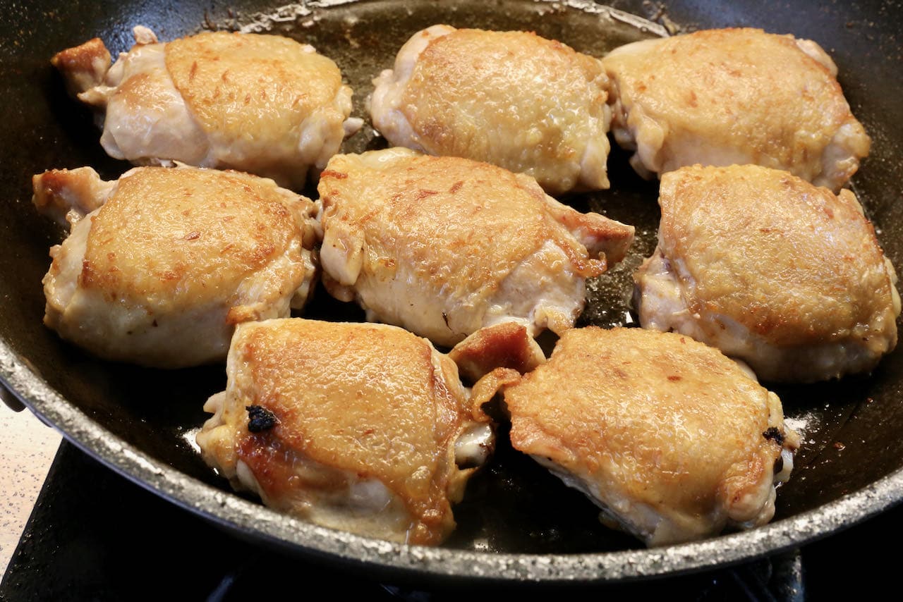 Begin cooking Ca Ri Ga by browning chicken thighs in a skillet until the skin is crispy.