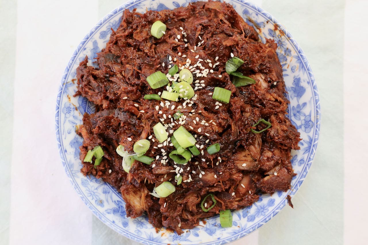 Serve Gochujang Pulled Pork garnished with sesame seeds and sliced scallions.