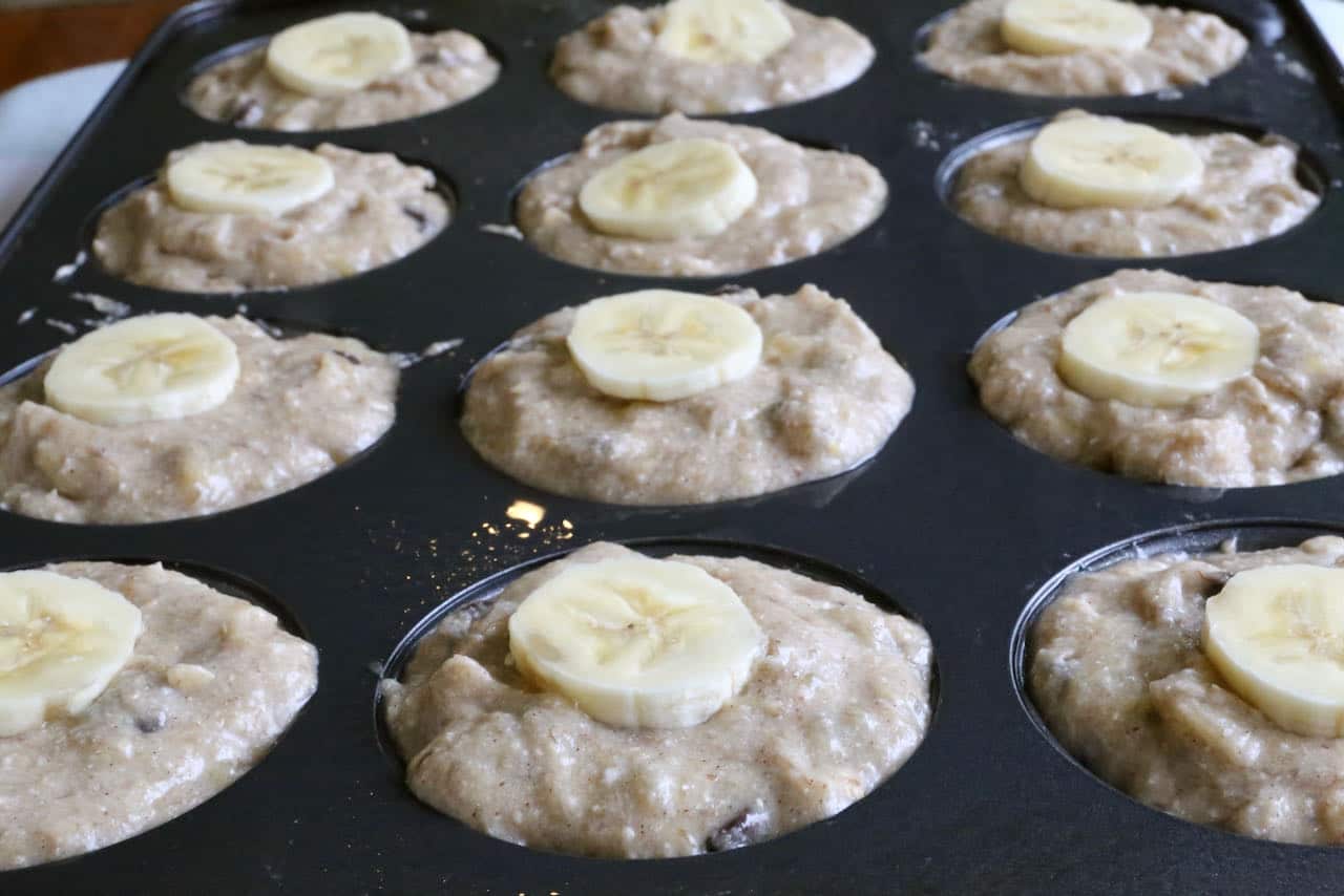 Fill greased tins with gluten free banana chocolate chip muffins batter and top with sliced banana.