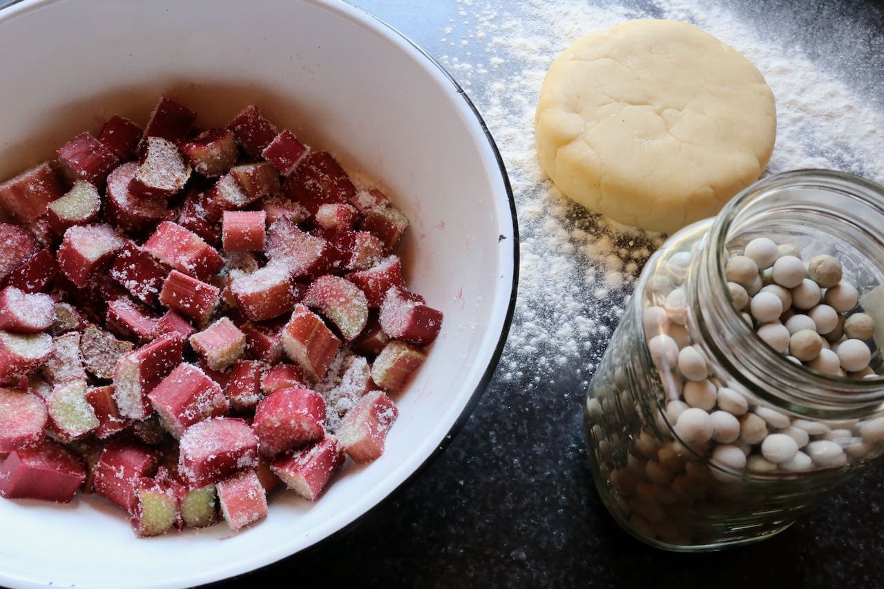 Toss rhubarb in sugar and roll out pie dough. Use pie weights to ensure the pastry does not puff up in the oven.