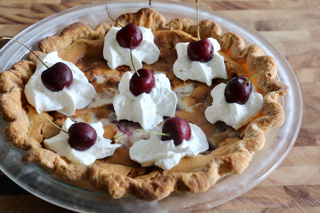 Decorate Cherry Custard Pie with whipped cream and fresh cherries.