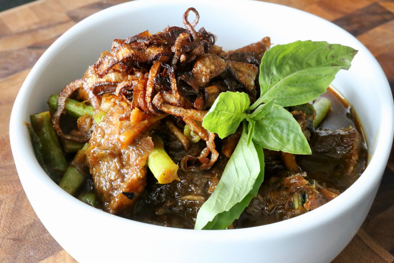 Serve Pork Belly Curry garnished with Thai basil and fried shallots.