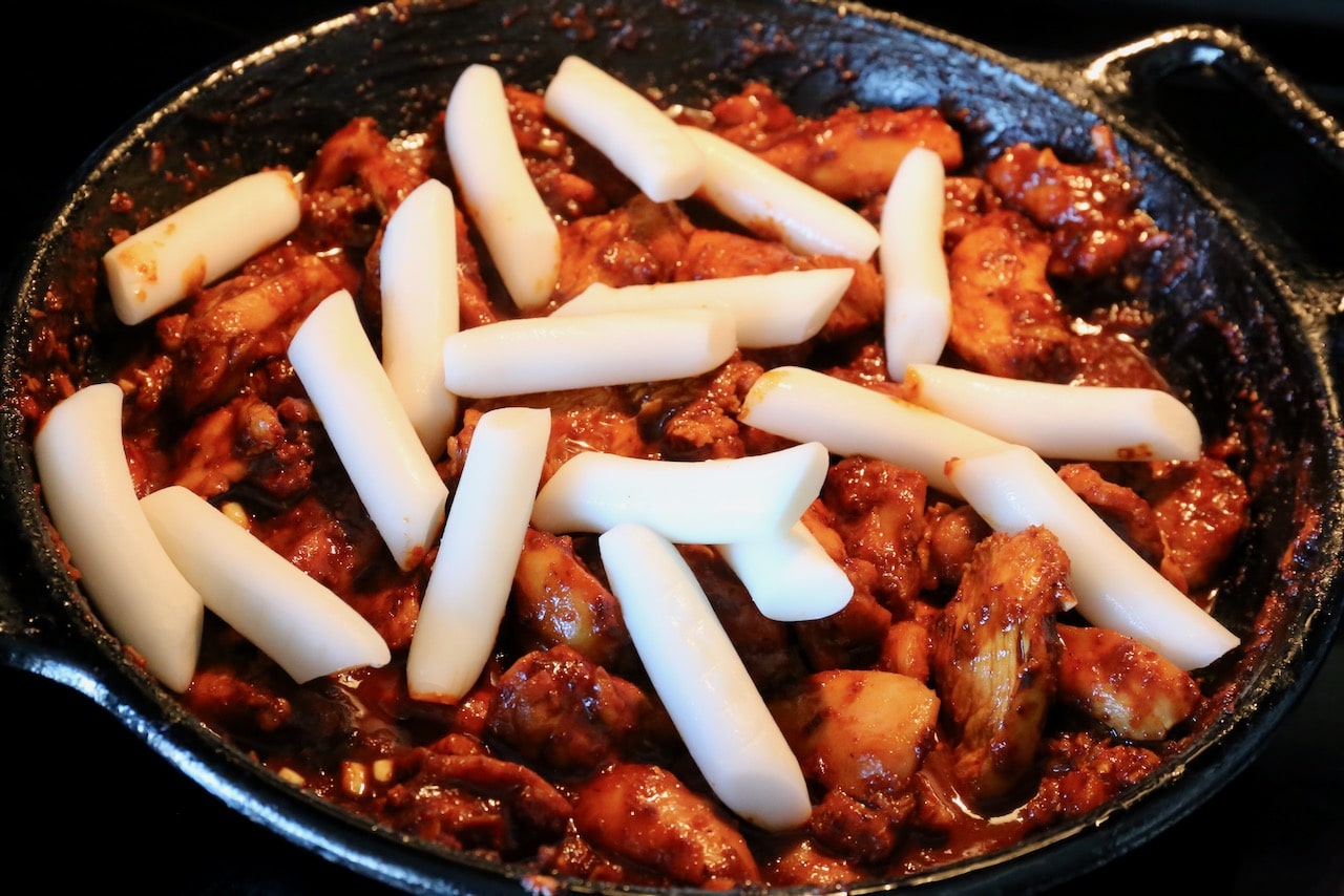 Cook Tteokbokki Korean rice cakes in a skillet with spicy chicken.