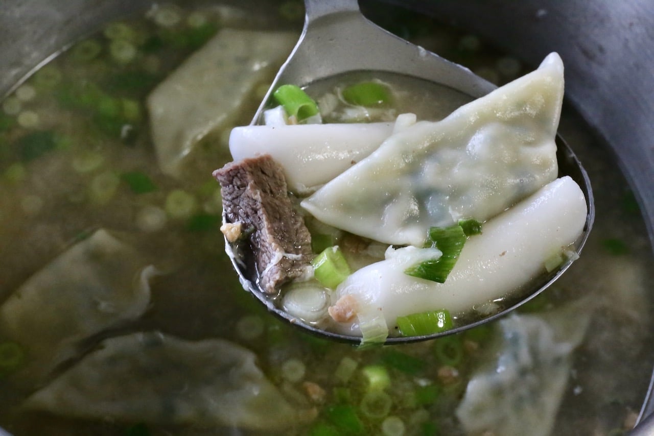 Use a ladle to serve Tteok Mandu Guk into bowls.
