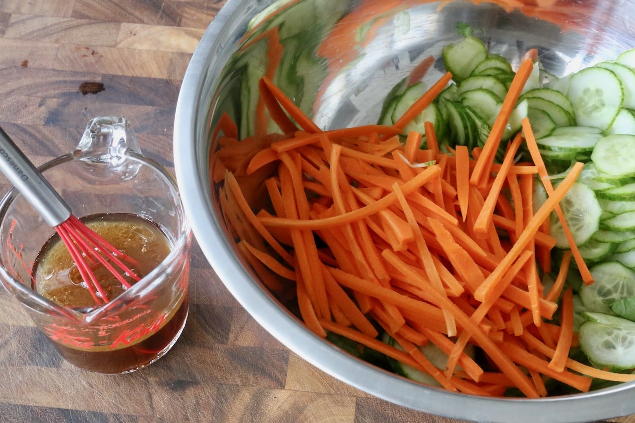 Toss salad dressing in a mixing bowl with chopped carrots and sliced cucumbers.
