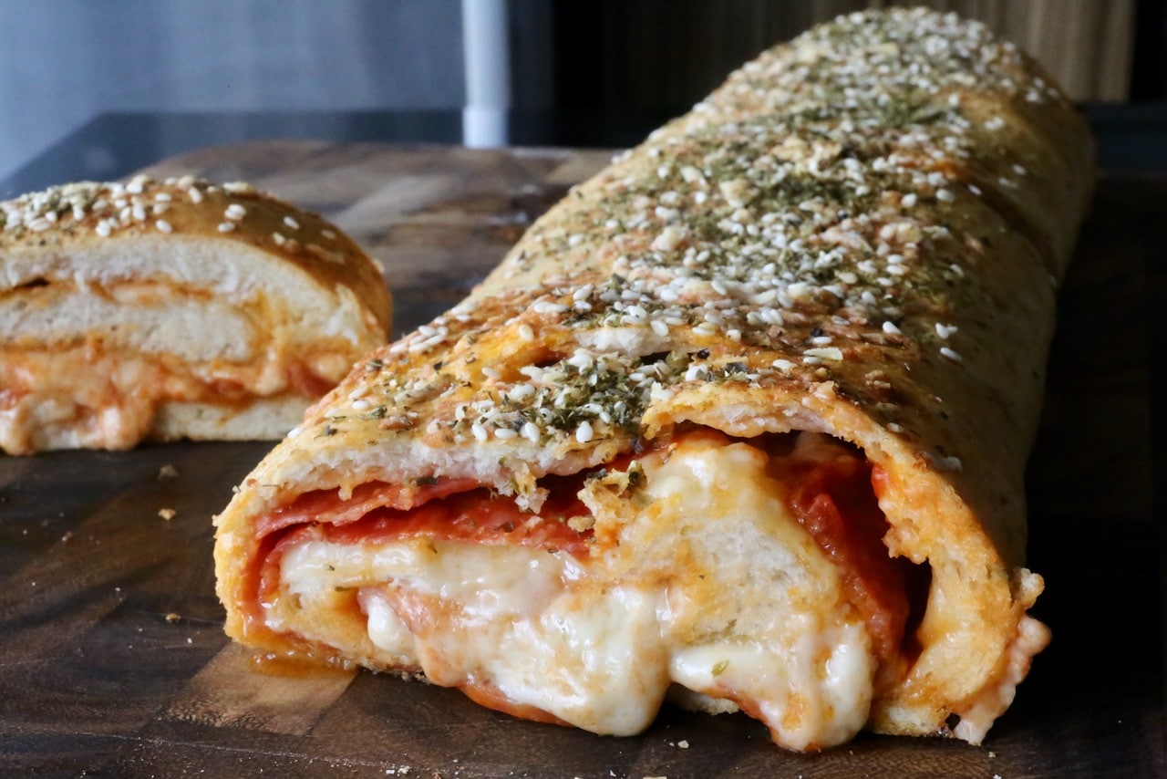 Our easy Stromboli Pizza recipe is sliced to reveal melted cheese and crispy meats.