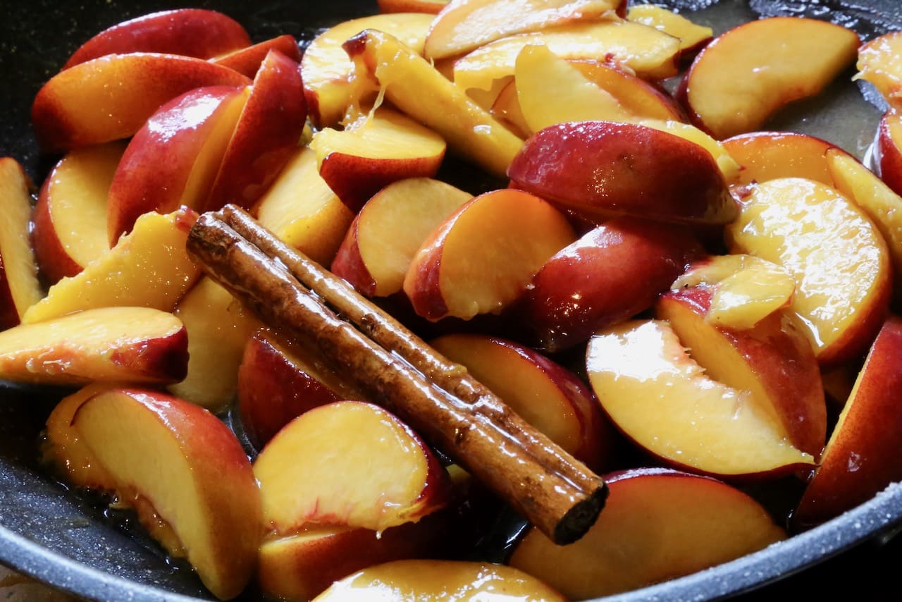 Stewed peaches are cooked in a skillet with spices like cinnamon.