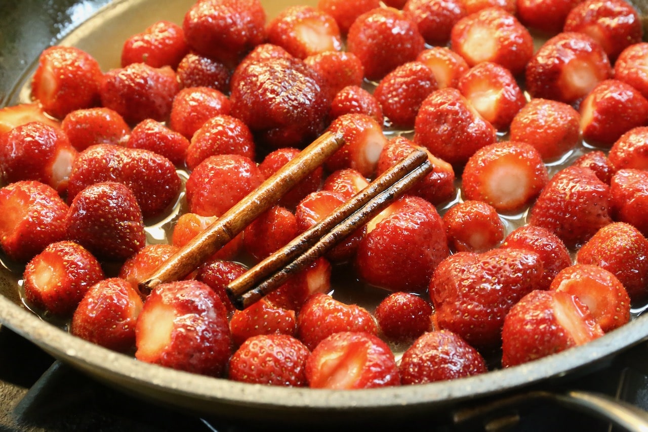 Poached strawberries are cooked in a skillet with spices like cinnamon.