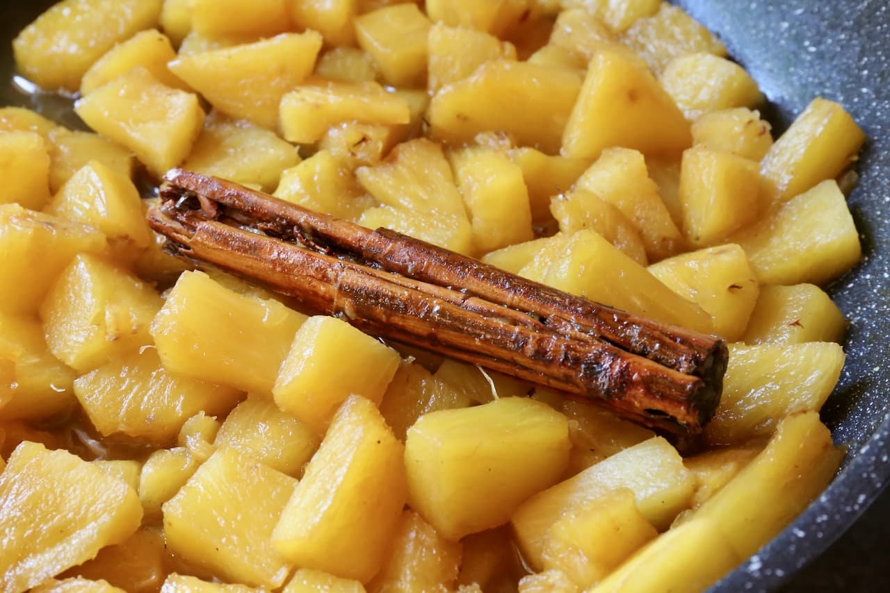 Stewed pineapple are cooked in a skillet with spices like cinnamon.